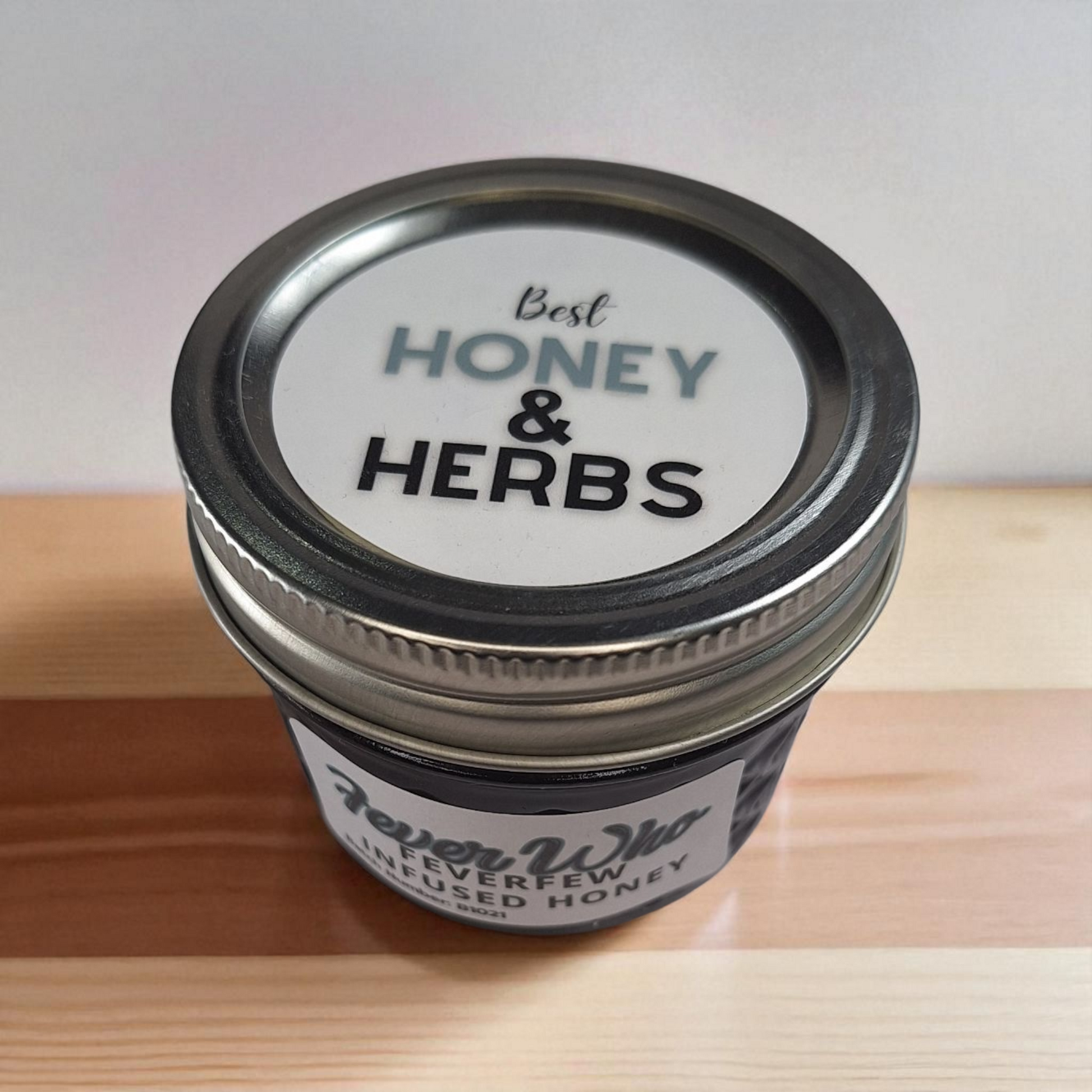 Top-down 4 oz jar of Feverfew Infused Honey on rustic wood; traditional herbal sweetener for warm teas and simple syrups.