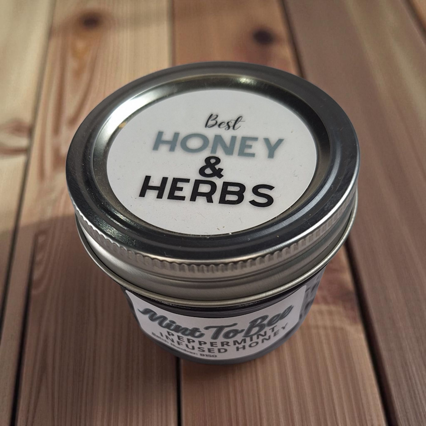 Top-view 4 oz Peppermint Leaf Infused Honey on a wooden board; refreshing herbal honey for hot cocoa, iced tea, and brownies.
