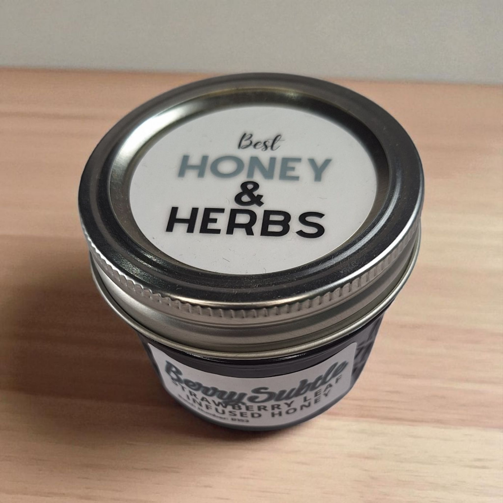 Top-down 4 oz Strawberry Leaf Infused Honey on warm wood; mild herbal honey for smoothies, oatmeal, and light teas.